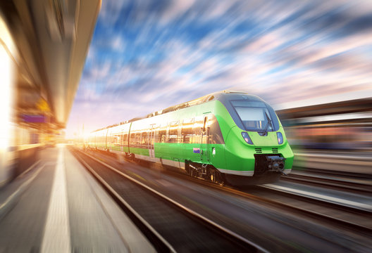 Fototapeta High speed train in motion at the railway station at sunset in Europe. Beautiful green modern train on the railway platform with motion blur effect. Industrial scene with passenger train on railroad