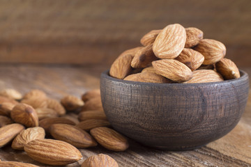 Almonds in a bowl against dark rustic wood background - Prunus dulcis