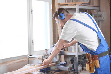 Focused carpenter sawing timber strip in workshop