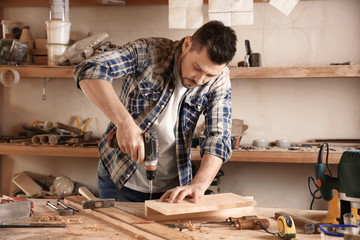 Carpenter driving screw nail into timber in workshop