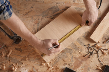 Carpenter marking measurements on piece of wooden board