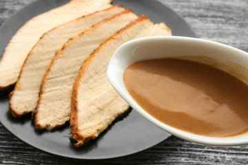 Turkey gravy in sauce boat over plate with sliced meat on table