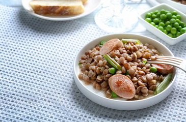 Plate with tasty lentil porridge, sausages, vegetables and fork on table