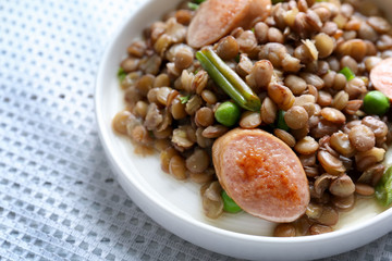 Plate with tasty lentil porridge, sausages and vegetables on table, closeup