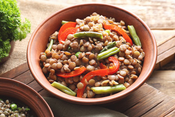 Plate with tasty lentil porridge, vegetables and wooden board on table, closeup
