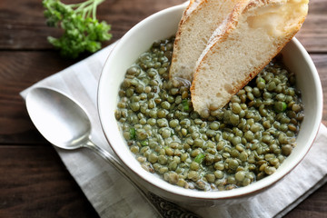 Bowl with tasty lentil dish and bread on wooden table, closeup