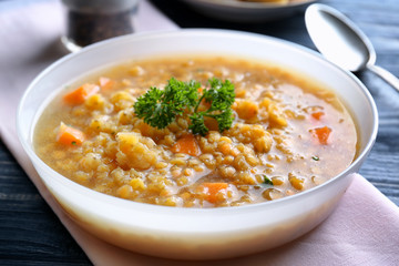 Plate with tasty lentil dish and napkin on wooden table, closeup