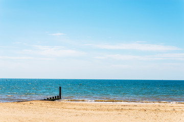 Dock pilings on a sandy beach, blue ocean and yellow sand, sunny hot day in seaside resort