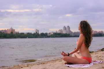 Fototapeta na wymiar Girl doing meditation and practicing yoga at a river coast in a city