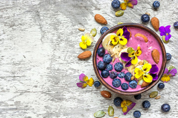 Obraz na płótnie Canvas bowl of homemade smoothie topped with fresh blueberries, nuts, chia and pumpkin seeds and flowers