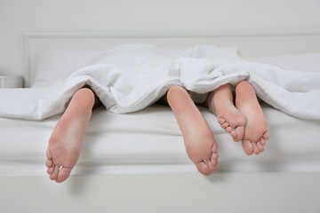 Bare feet of man and woman lying under blanket after sex