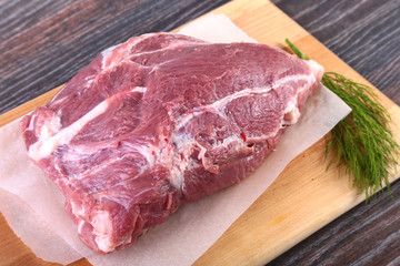 Raw pork steaks on wooden board with herbs, garlic and spices ready for cooking. Selective focus.