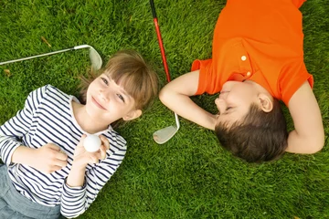 Photo sur Aluminium Golf Enfants mignons avec ballon et conducteurs allongés sur un terrain de golf