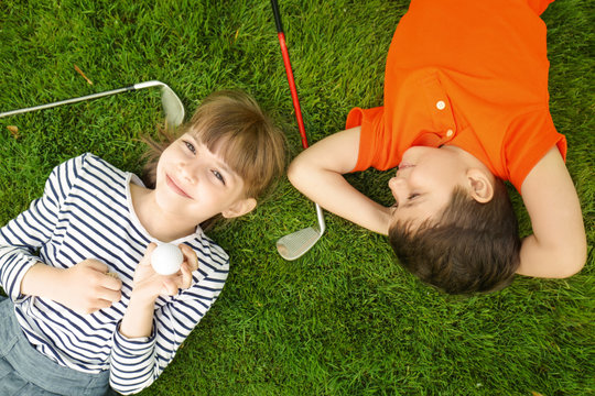 Cute children with ball and drivers lying on golf course