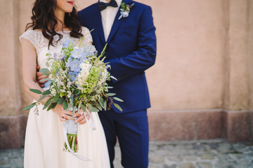 Love on wedding day. Caucasian bride and groom hugging and holding a wedding bouquet in their hands.