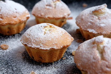 heap of cupcakes with sugar powder and raisins on black background