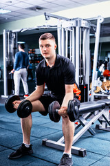 Handsome young sportive man in sportswear lifting some weights