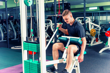 Sportive young man in sportswear doing exercise on a machine