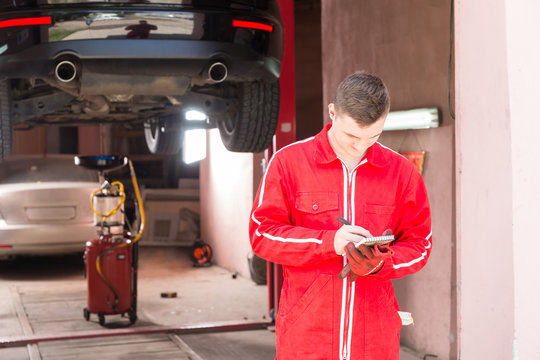 Male motor mechanic standing making notes in front of a black sedan elevated