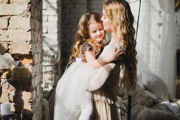 Mother and daughter hugging and playing together. Pretty little girl on beautiful woman's hands. Girls in lace dresses playing in decorated room. Family weekend, beauty day, having fun, love concept.