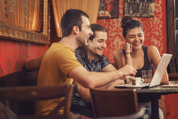 Group of friends browsing internet, doing a project on a laptop in a coffee shop