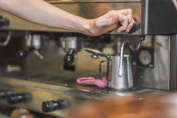 Young man bartender frothing milk foam on a barista machine