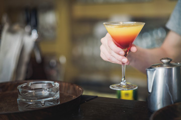 Young bartender making a colorful cocktail, pouring alcohol in a cocktail glass