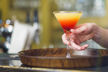Young bartender making a colorful cocktail, pouring alcohol in a cocktail glass