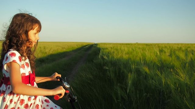 Child with a bicycle outdoors. Girl riding a bicycle on a wheat field.