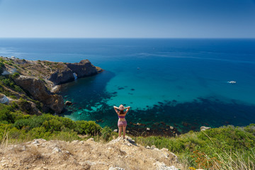 Obraz premium Beautiful woman standing on a rock above the Black sea and looking at calm and deep blue water. Feel free to explore, adventure and discovery nature treasure of nature.From the back. Top view.