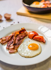Fried chicken eggs with crispy bacon and tomatoes against white background