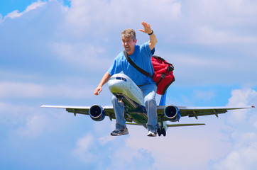 A happy man with a red duffel bag is waving as he flies through the air riding on an airplane like...