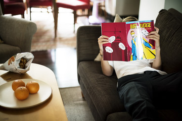 Young caucasian man lying on the couch reading cartoon