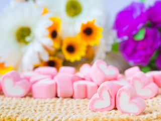 Obraz na płótnie Canvas Closeup of sweet marshmallow in the shape of heart on wooden plate and flower at background. Concept about love and relationship. (Soft Style for Background)