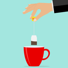 The hand holds a teabag over the cup. Brew tea