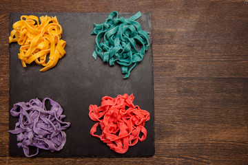 Colorful tagliatelle on black plate on table. Creative food concept top view, free space on wooden background