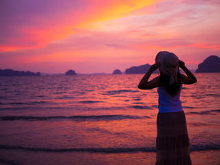 Silhouette of woman wearing hat with open arms under the sunrise near the sea. Summer concept.