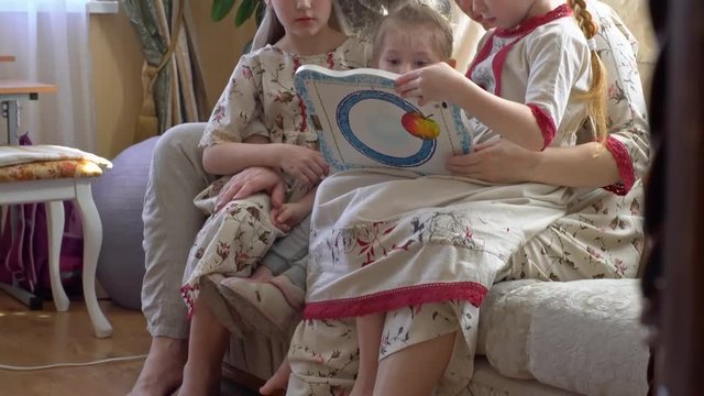 Tilt up of little sisters and their younger brother in traditional Russian clothing sitting on sofa with mother and senior father with grey bushy beard and playing on tablet while chatting