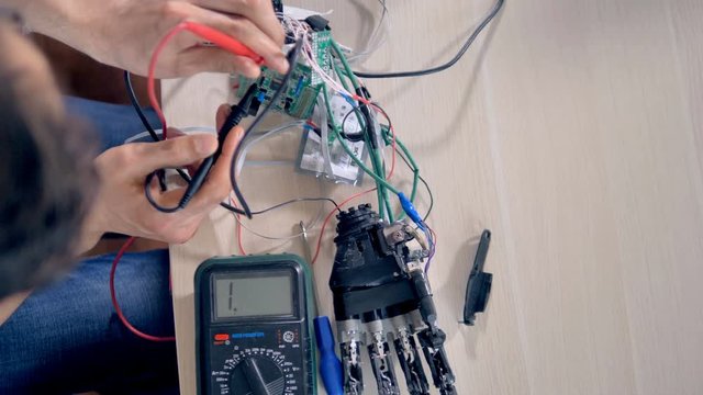Engineer working with a bionic hand and a multimeter.
