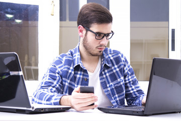 Young man at office with cellphone and laptop