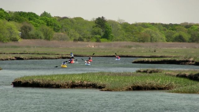 Zoomed shot of paddle boarder and kayaking group making their way up scorton creek through salt water marsh in Sandwich Cape Cod