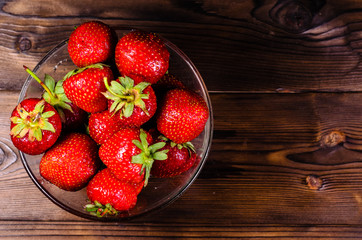 Ripe strawberries in glass bowl on wooden table. Top view