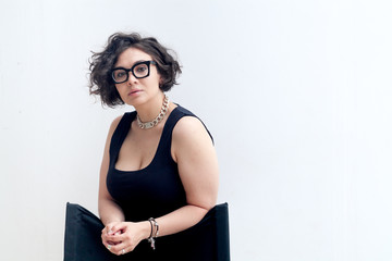 Portrait of young plus size model with dark curvy hair wearing fashionable black glasses and...