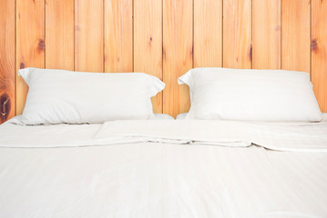 Fototapeta na wymiar A white bed with 2 pillows on wooden wall room background