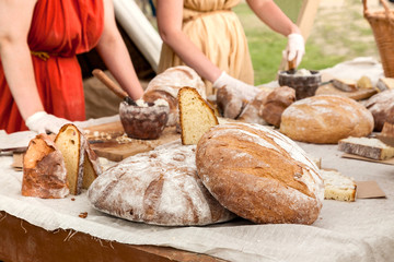 Big round bread loafs on wooden table with few persons on a background