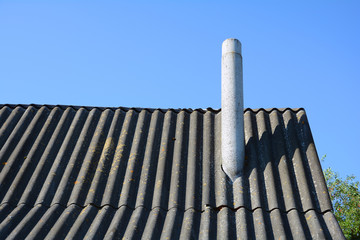Old roof asbestos roof slates and chimney against blue sky