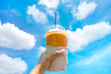 Hand holding coffee smoothie in plastic cup and blue sky.