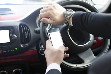 Naklejka premium Close-up of a man's hand holding a smartphone. Businessman texting while sitting in a car. Holding a steering wheel and using a mobile phone.
