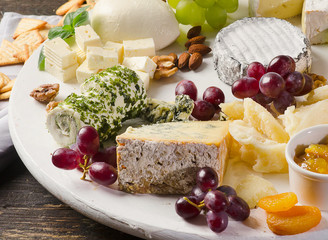 Cheese plates served with grapes, jam,  and nuts on a wooden board.