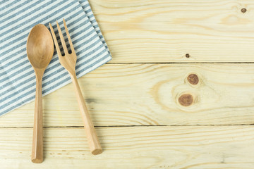 Tablecloth, wooden spoon, fork on wood table background.